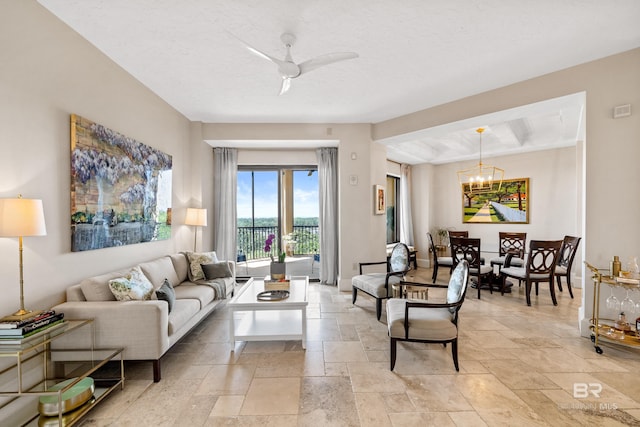 living room featuring ceiling fan with notable chandelier and stone tile flooring