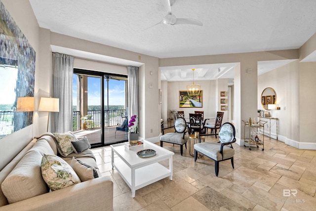 living room with a textured ceiling, baseboards, ceiling fan with notable chandelier, and stone tile flooring