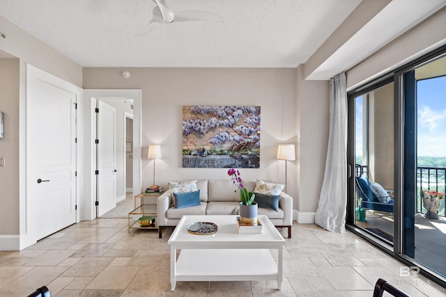 living area featuring baseboards, ceiling fan, a textured ceiling, and stone tile floors