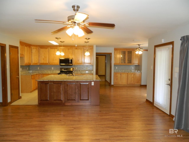 kitchen with light stone counters, decorative backsplash, stainless steel appliances, hanging light fixtures, and light hardwood / wood-style flooring