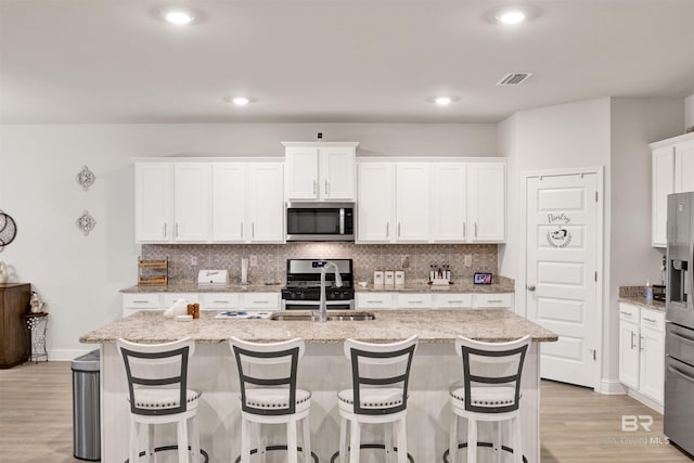 kitchen with a center island with sink, stainless steel appliances, visible vents, decorative backsplash, and a sink