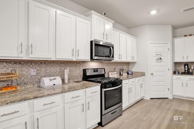 kitchen with white cabinetry, decorative backsplash, light hardwood / wood-style floors, stainless steel appliances, and light stone countertops