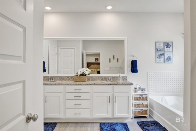 bathroom with double vanity, a bath, wood finished floors, a sink, and recessed lighting