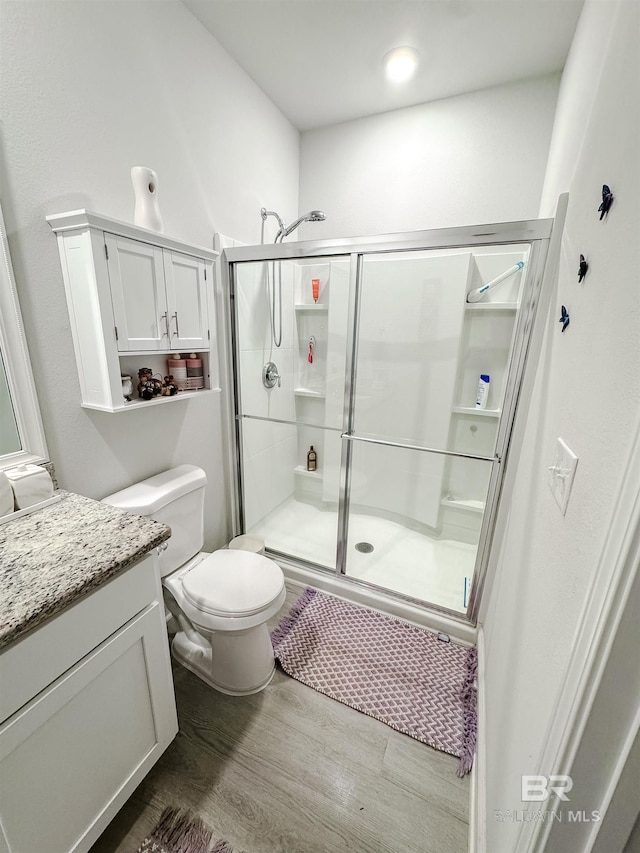 bathroom featuring toilet, wood finished floors, a shower stall, and vanity