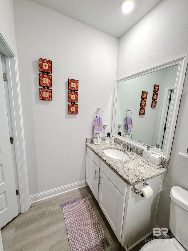 half bath featuring toilet, wood finished floors, vanity, and baseboards