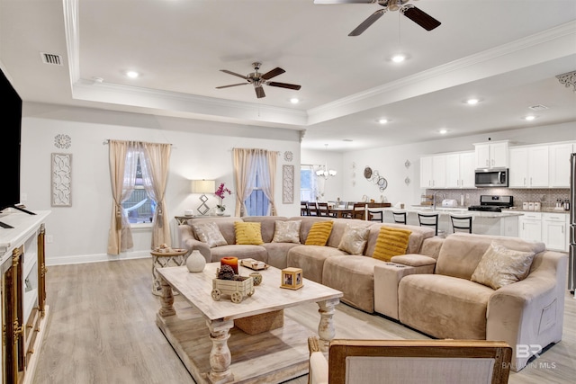 living area with a tray ceiling, crown molding, a wealth of natural light, visible vents, and light wood-type flooring