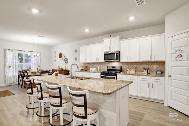 kitchen with stainless steel appliances, a sink, light wood-style floors, backsplash, and a kitchen bar