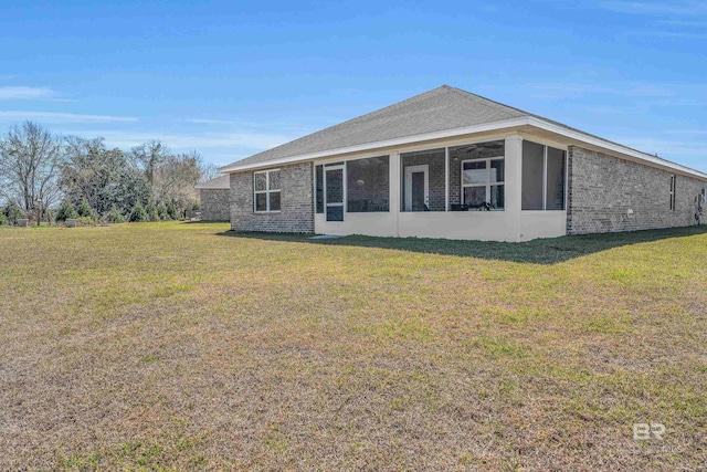 view of front of house featuring brick siding, roof with shingles, a front yard, and a sunroom