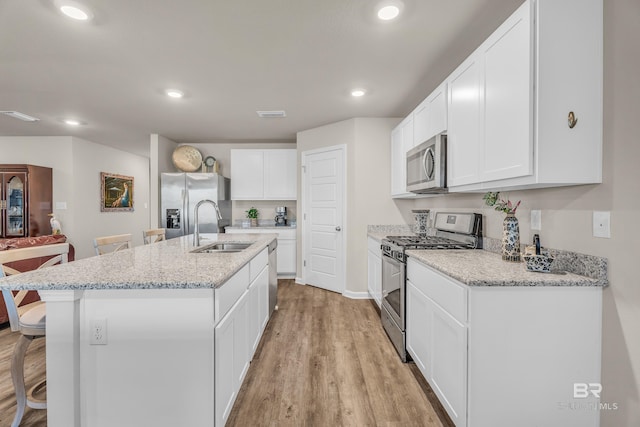 kitchen with a breakfast bar, appliances with stainless steel finishes, a kitchen island with sink, a sink, and light wood-type flooring