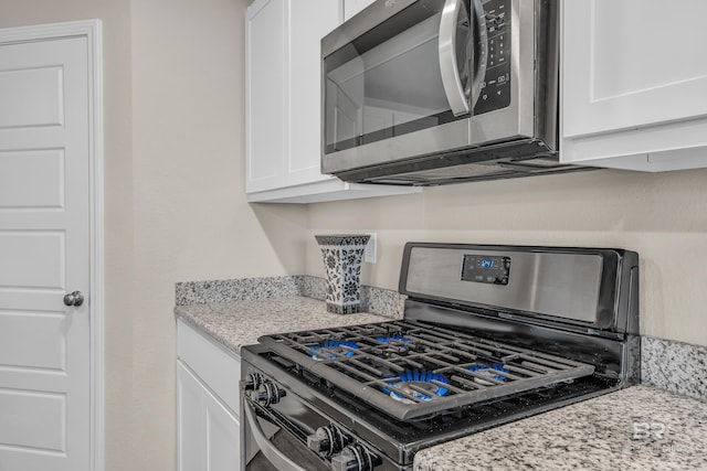 kitchen with stainless steel appliances, light stone countertops, and white cabinets