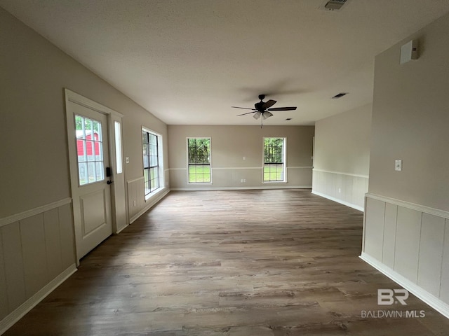 unfurnished room featuring a ceiling fan, wainscoting, a decorative wall, and wood finished floors