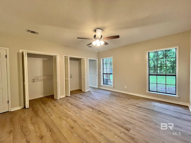 unfurnished bedroom with visible vents, a textured ceiling, wood finished floors, and two closets