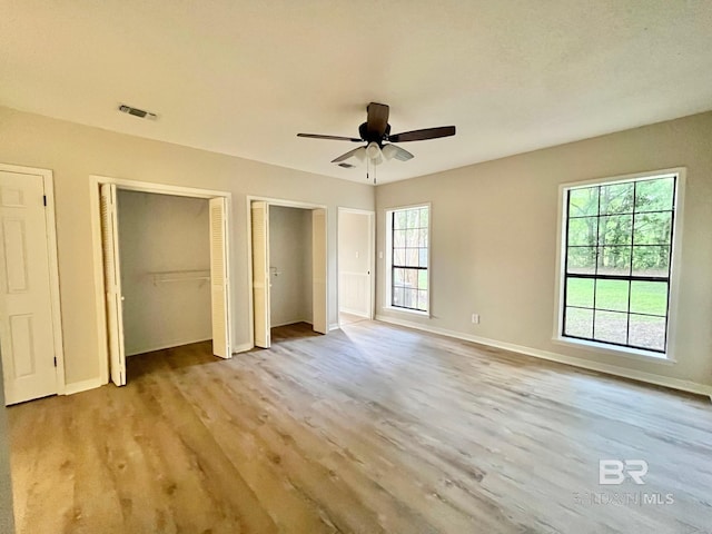 unfurnished bedroom with visible vents, baseboards, multiple closets, and wood finished floors