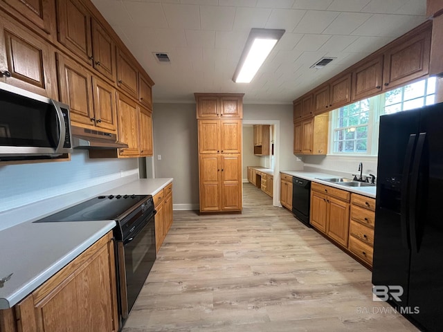 kitchen with visible vents, light wood-style floors, under cabinet range hood, a sink, and black appliances