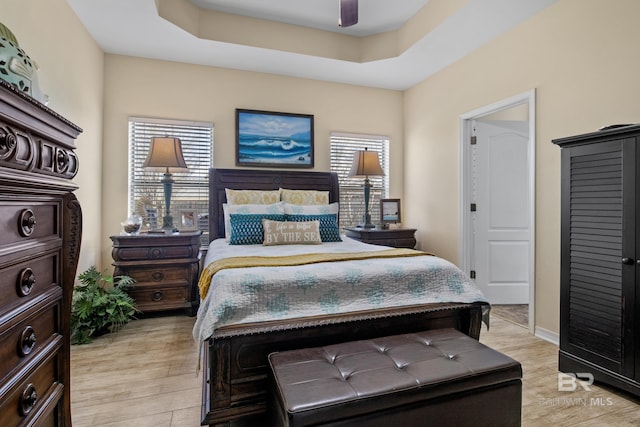 bedroom featuring ceiling fan, light hardwood / wood-style floors, and a tray ceiling