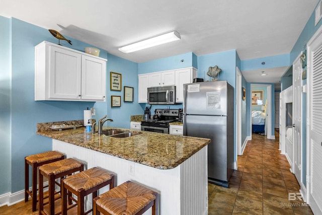 24568 Perdido Beach Blvd Unit 502, Orange Beach, AL 36561 - kitchen featuring stainless steel appliances, a peninsula, dark stone counters, white cabinetry, and a kitchen bar