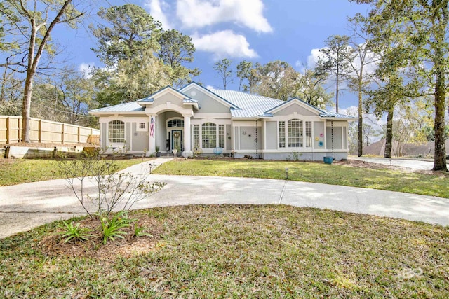 view of front of home with a front yard, fence, a standing seam roof, stucco siding, and metal roof