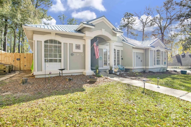 view of front of home featuring a front yard, fence, a standing seam roof, stucco siding, and metal roof