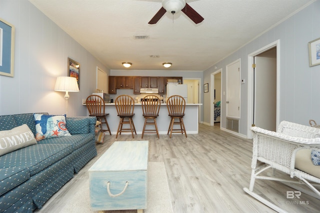 living room with visible vents, a ceiling fan, light wood-style flooring, and crown molding