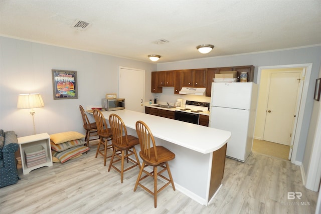 kitchen featuring a sink, under cabinet range hood, light wood-type flooring, visible vents, and white appliances