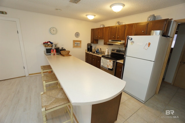 kitchen featuring under cabinet range hood, a kitchen bar, light countertops, stainless steel electric stove, and freestanding refrigerator