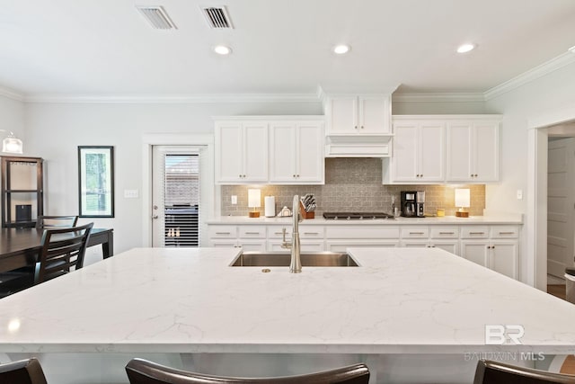 kitchen with white cabinetry, premium range hood, a kitchen island with sink, and sink