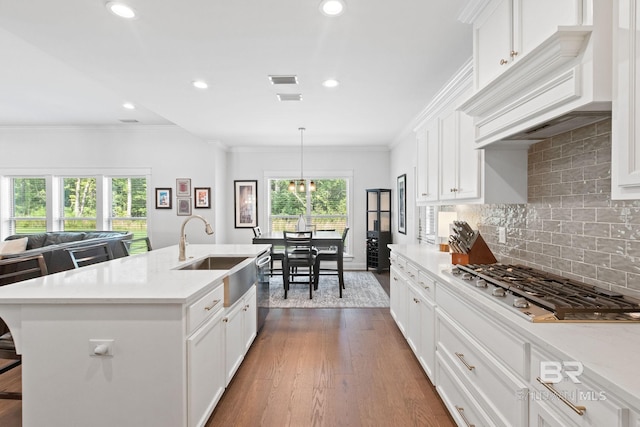 kitchen with a center island with sink, hanging light fixtures, decorative backsplash, dark wood-type flooring, and custom range hood