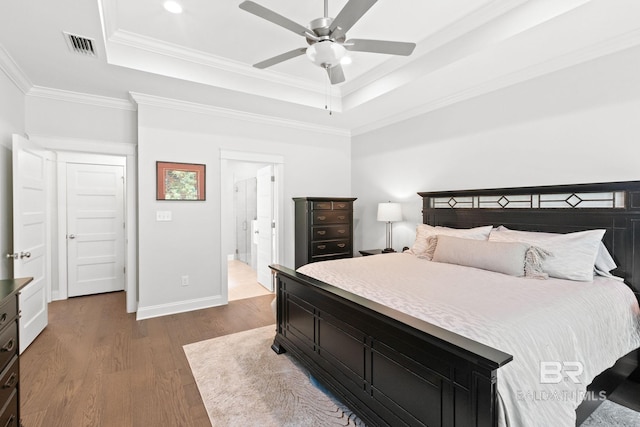 bedroom with a tray ceiling, ensuite bath, crown molding, dark wood-type flooring, and ceiling fan