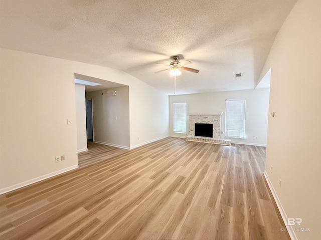 unfurnished living room featuring ceiling fan, light wood-type flooring, a textured ceiling, and vaulted ceiling