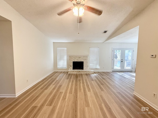 unfurnished living room with ceiling fan, french doors, vaulted ceiling, a textured ceiling, and a fireplace