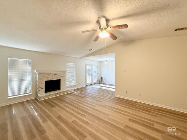 unfurnished living room with lofted ceiling, french doors, ceiling fan, a textured ceiling, and a fireplace