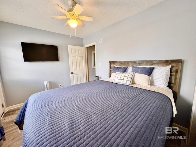 bedroom with ceiling fan, a textured ceiling, baseboards, and wood finished floors