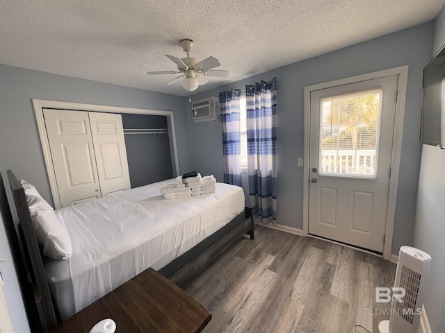 bedroom featuring wood-type flooring, a textured ceiling, a closet, a wall unit AC, and ceiling fan