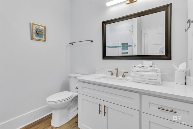bathroom featuring toilet, wood finished floors, vanity, baseboards, and walk in shower