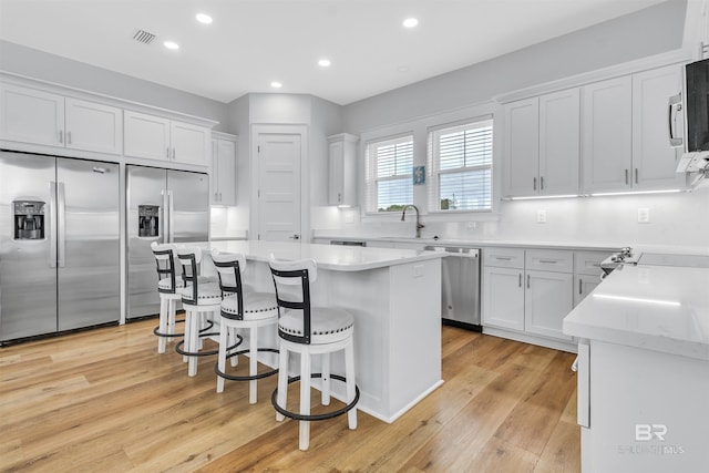 kitchen featuring stainless steel appliances, a kitchen island, white cabinets, light countertops, and a kitchen bar