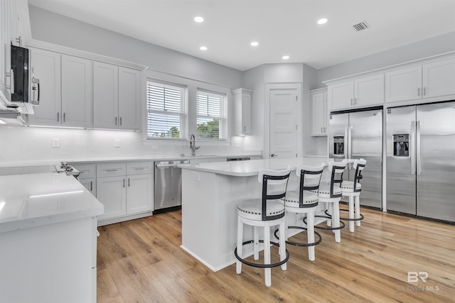 kitchen featuring stainless steel appliances, white cabinetry, a sink, a kitchen island, and a kitchen breakfast bar