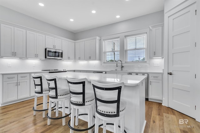 kitchen with a center island, light countertops, stainless steel microwave, white cabinets, and a sink