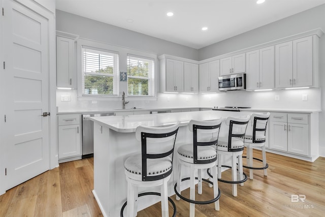 kitchen with a center island, stainless steel appliances, light countertops, white cabinetry, and a sink