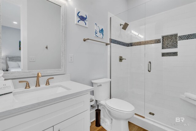 bathroom featuring toilet, a stall shower, wood finished floors, and vanity