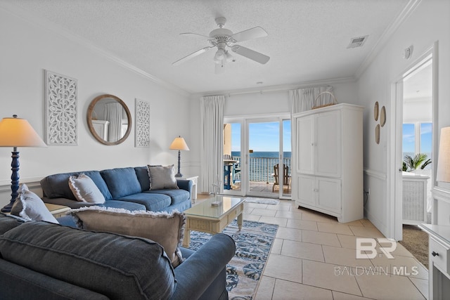 living room featuring ceiling fan, a water view, light tile floors, a textured ceiling, and ornamental molding