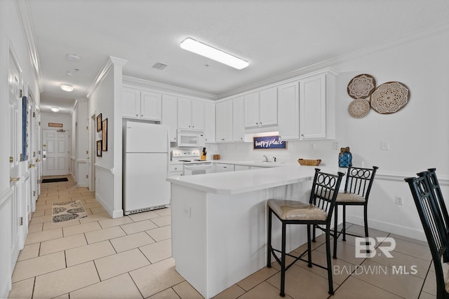 kitchen with light tile floors, a kitchen bar, white appliances, white cabinetry, and crown molding