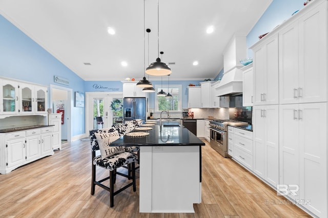 kitchen with high end appliances, decorative light fixtures, a kitchen island with sink, and white cabinets