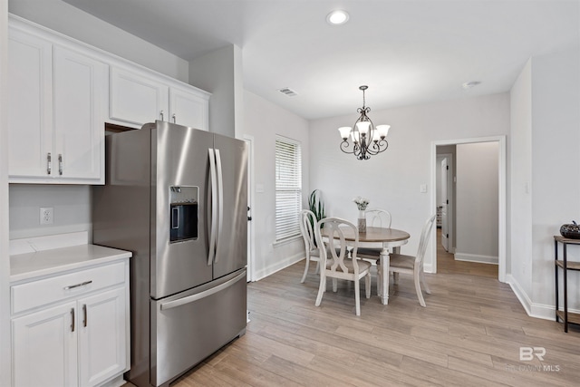 kitchen with light wood finished floors, white cabinetry, stainless steel fridge, a notable chandelier, and baseboards