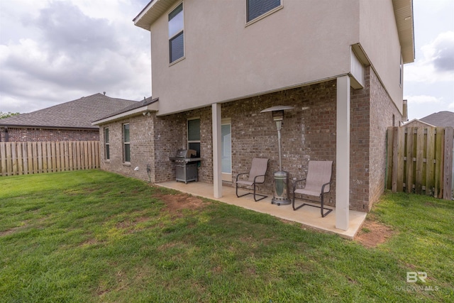 back of house featuring a yard, a patio, brick siding, and a fenced backyard