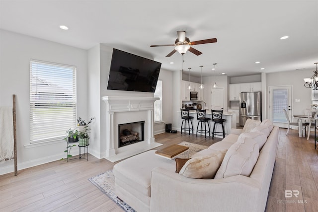 living area with light wood finished floors, ceiling fan with notable chandelier, and plenty of natural light