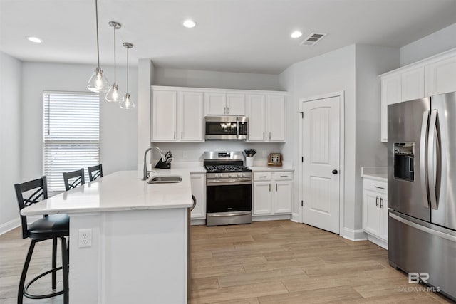 kitchen featuring light wood finished floors, a sink, a kitchen bar, a peninsula, and appliances with stainless steel finishes