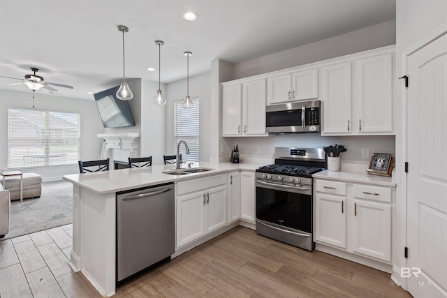kitchen with a peninsula, a sink, open floor plan, ceiling fan, and appliances with stainless steel finishes
