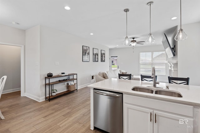 kitchen featuring stainless steel dishwasher, light wood finished floors, a sink, open floor plan, and light countertops