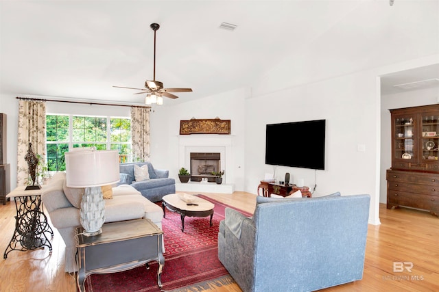 living room with light hardwood / wood-style floors, a tiled fireplace, ceiling fan, and lofted ceiling