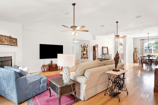 living room featuring ceiling fan, a tile fireplace, lofted ceiling, and light wood-type flooring